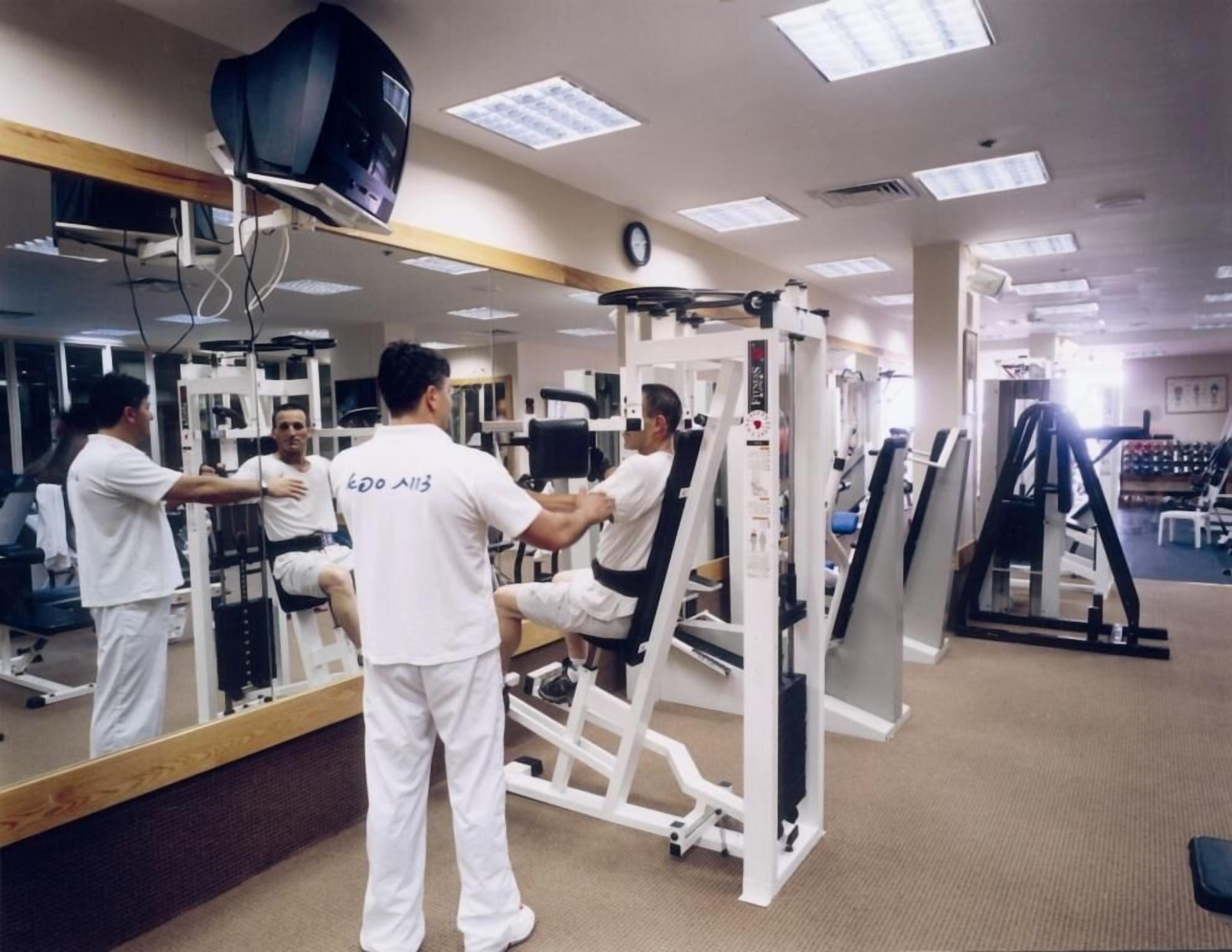 A gym with exercise equipment, a large mirror, and a clock on the wall.