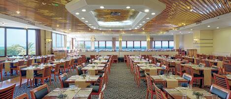 A large dining area with multiple tables and chairs, a patterned carpet, and a ceiling with a unique design.