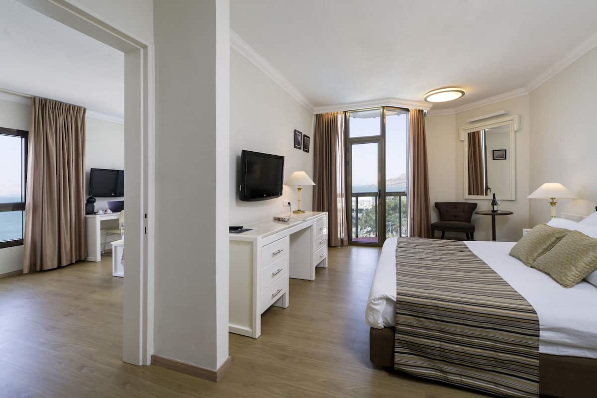 A hotel room with a bed, desk, chair, TV, and a balcony with curtains.