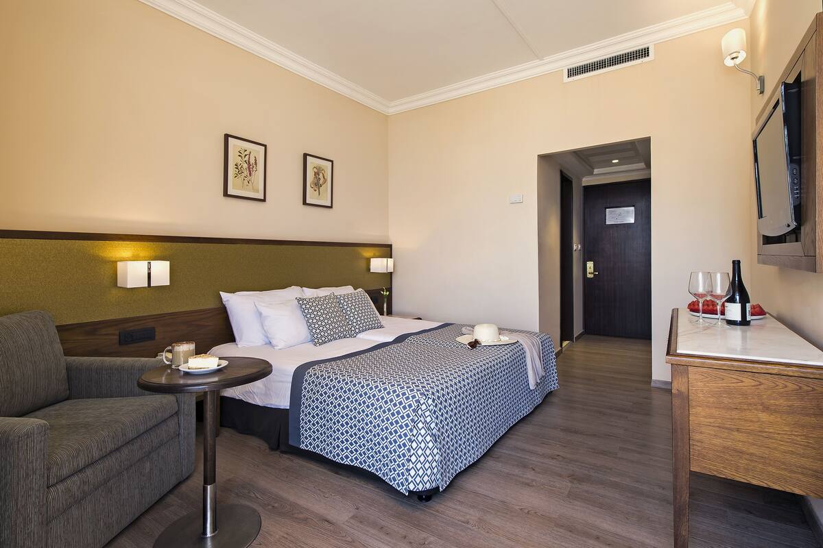 A hotel room with a bed, a sofa, a small table with a drink and a plate of fruit, and a TV on a stand.