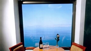 A table with a bottle and glasses, a decorative item, and a view of the ocean through a window. - Caesar Premier Tiberias (Tiberias)