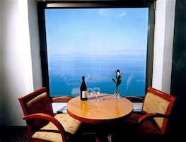 Una mesa con una botella y vasos, un adorno y vista al océano a través de una ventana.