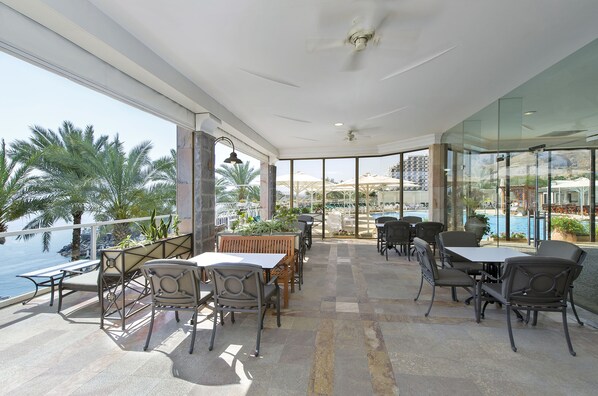 A spacious outdoor seating area with tables and chairs, overlooking a pool and palm trees.