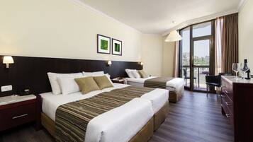A hotel room with two beds, a desk, and a chair. There are two bedside tables with lamps and a window with curtains.