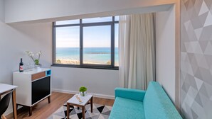 Una sala de estar moderna con vista a la playa, una mesita con aperitivos, un sofá y un televisor.