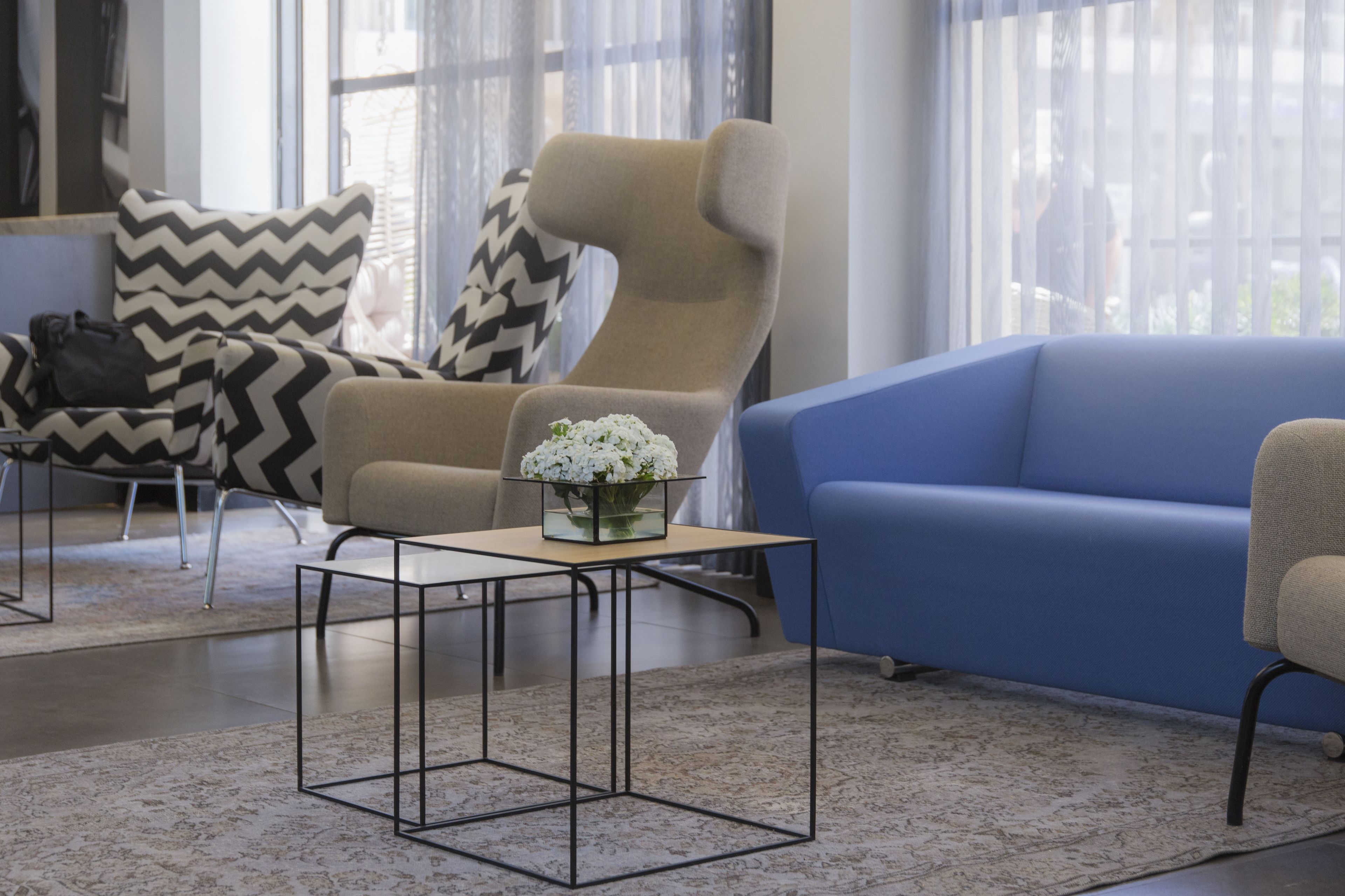 Un salon moderne avec un canapé bleu, un fauteuil beige et une chaise à motifs noir et blanc. On y trouve une petite table sur laquelle est posé un vase de fleurs.