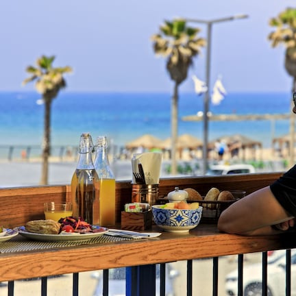 A balcony with a table set for breakfast overlooking a beach.