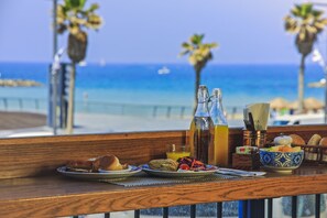 Una mesa de desayuno con vista al océano, que incluye pan, un tazón de fruta y una botella de jugo.