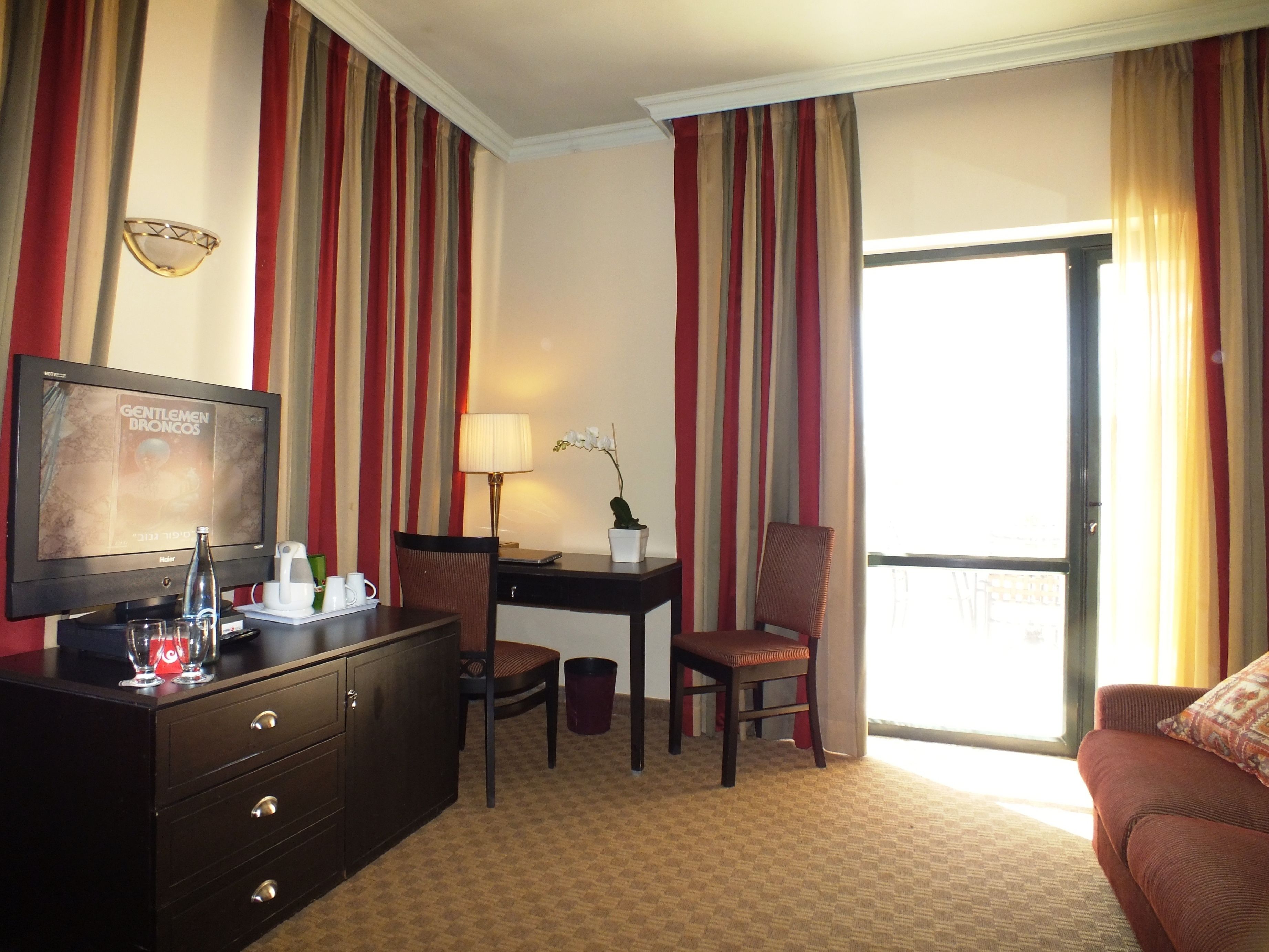 A hotel room with a television, desk, chair, and a sofa.