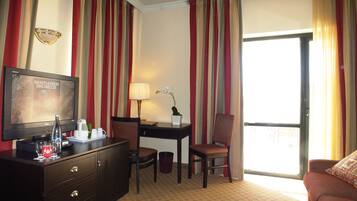 A hotel room with a television, desk, chair, and a sofa.