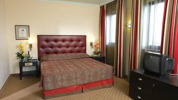 Una habitación de hotel con una cama grande, un televisor sobre una cómoda y una mesita de noche con una lámpara y flores.