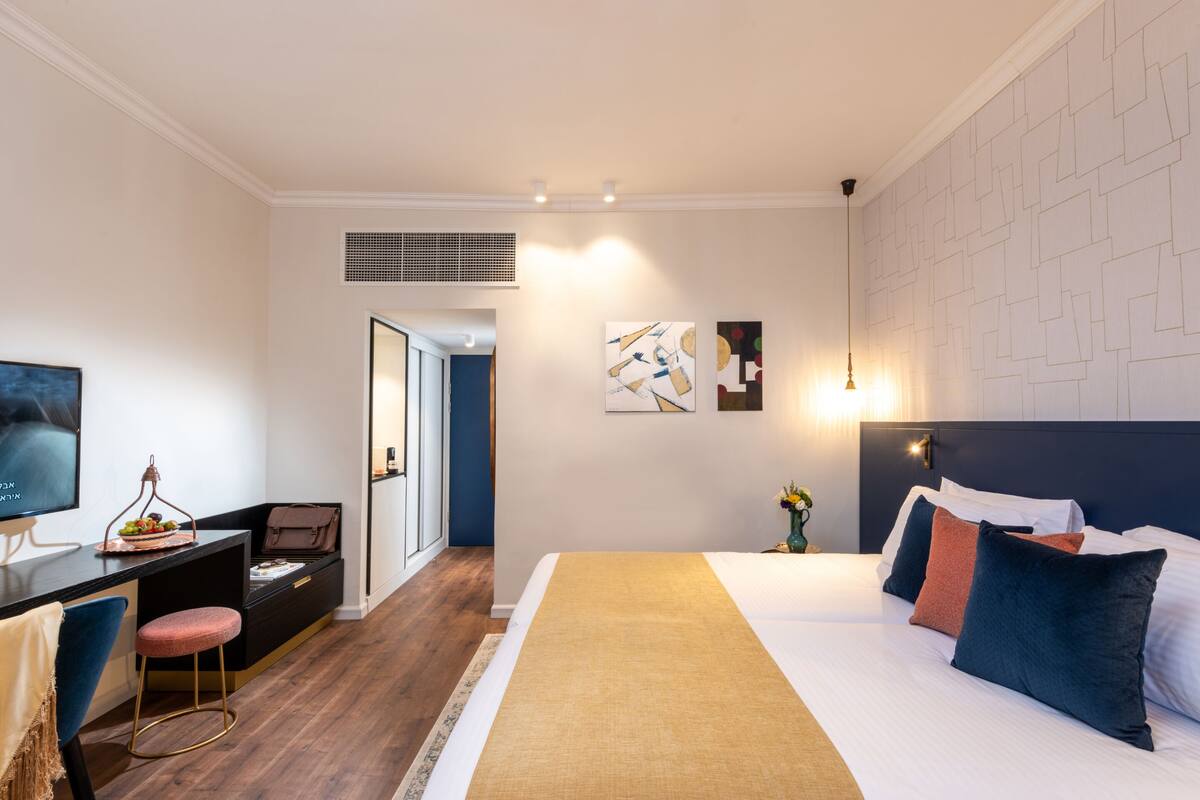 A modern hotel room with a bed, desk, and chair, a television, and artwork on the walls.