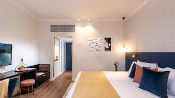 Une chambre d’hôtel moderne équipée d’un lit, d’un bureau et d’une chaise, d’une télévision et d’œuvres d’art accrochées aux murs.