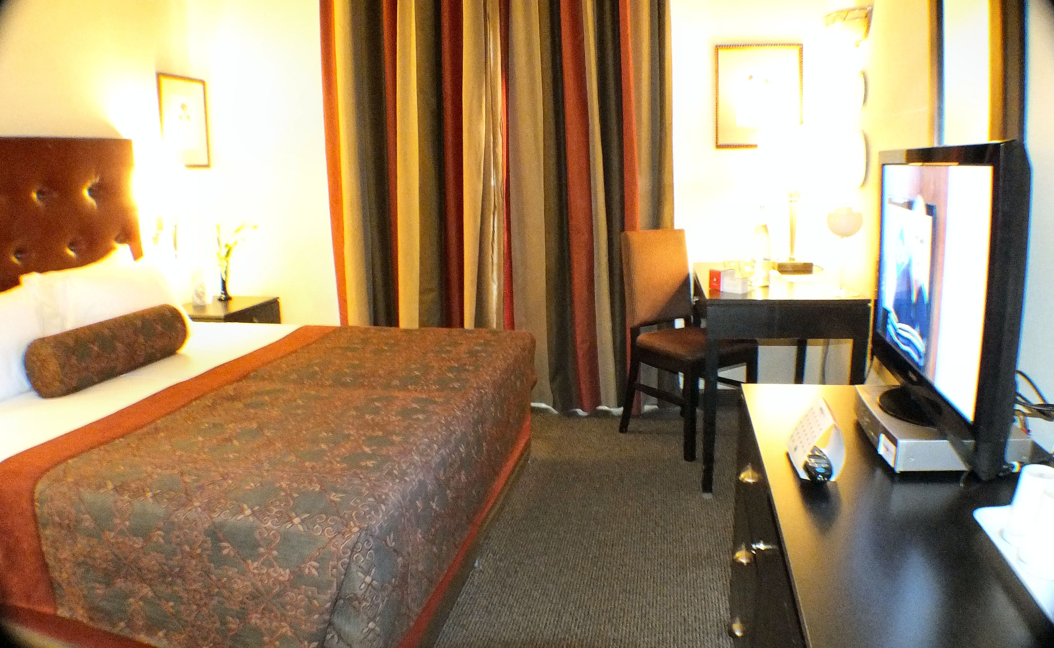 Ein Hotelzimmer mit Bett, Schreibtisch, Sessel, Fernseher und Vorhängen.