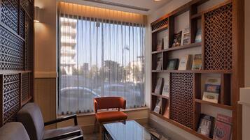 Una habitación moderna con una mesa de vidrio, dos sillas, una estantería y un amplio ventanal con cortinas.
