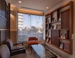 Una habitación moderna con una mesa de vidrio, dos sillas, una estantería y un amplio ventanal con cortinas.