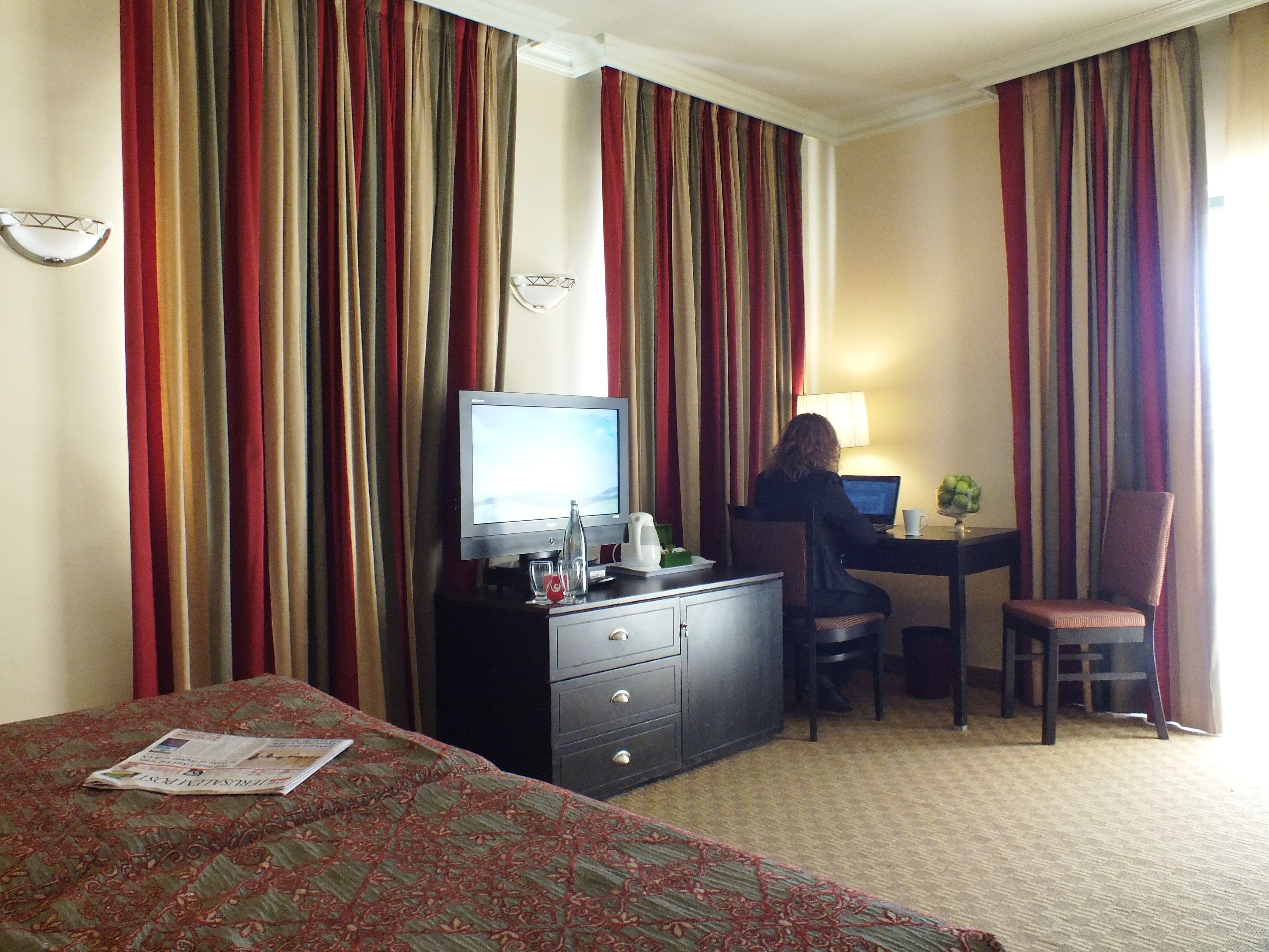 Una habitación de hotel con cama, escritorio, computadora, silla y televisión.
