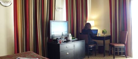 A hotel room with a bed, a desk with a computer, a chair, and a television.