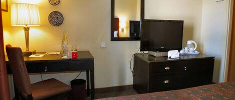 Una habitación de hotel con cama, escritorio con lámpara, televisor y cafetera.
