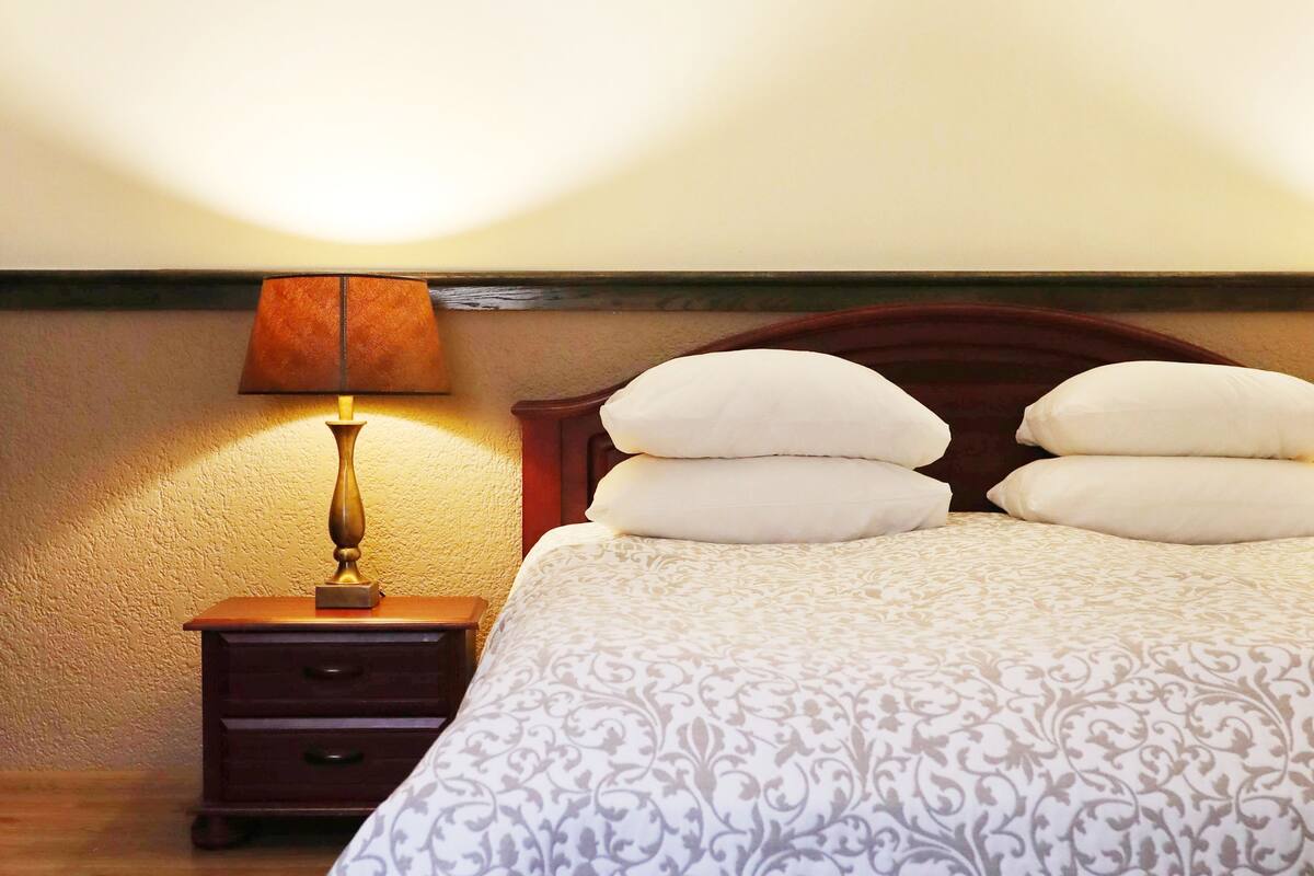A neatly made bed with a patterned bedspread, a bedside lamp, and two pillows.
