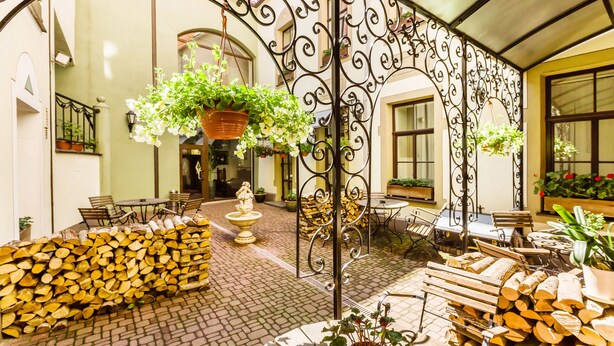 Un patio con un arco de metal, mobiliario de madera y plantas en macetas.