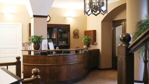 Una zona de recepción con mostrador de madera, plantas en macetas, un reloj y un candelabro.