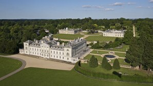 A large, historic building with symmetrical architecture, expansive lawns, and a formal garden layout.