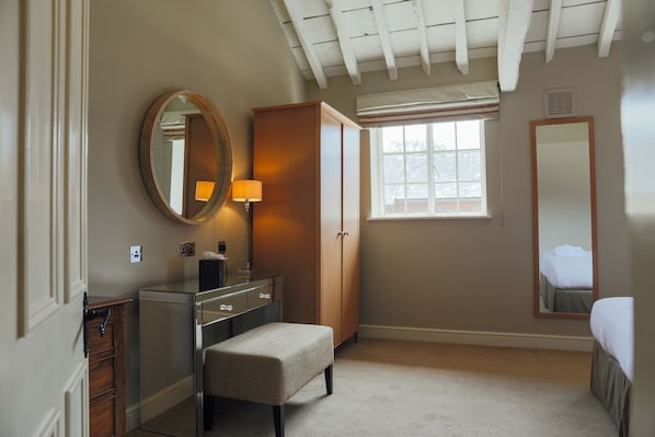 A bedroom with a bed, a dresser, a vanity with a mirror, and a window. - The Woburn Hotel (Milton Keynes)