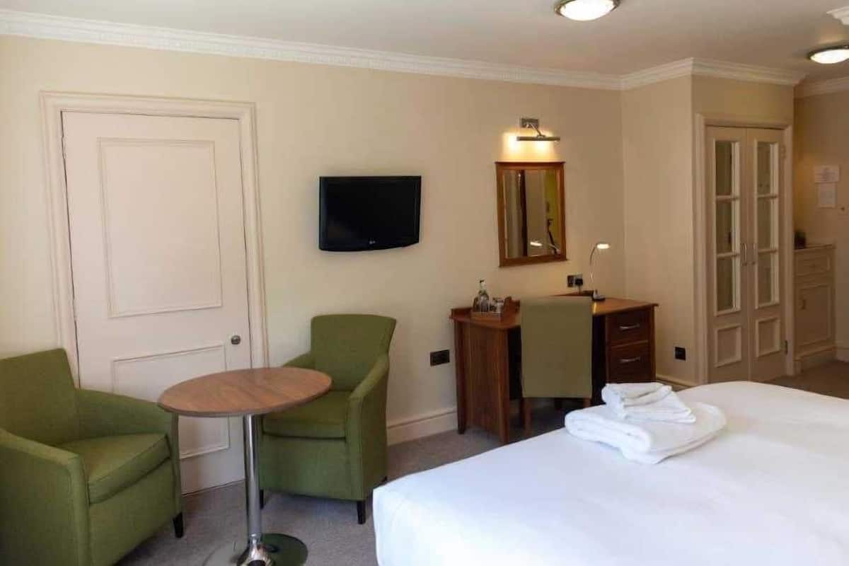 Habitación de hotel con una cama, un escritorio con una silla, una mesita redonda pequeña, un televisor y un espejo.