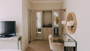 A hotel room with a television, a mirror, a vanity, and a door leading to a bathroom.