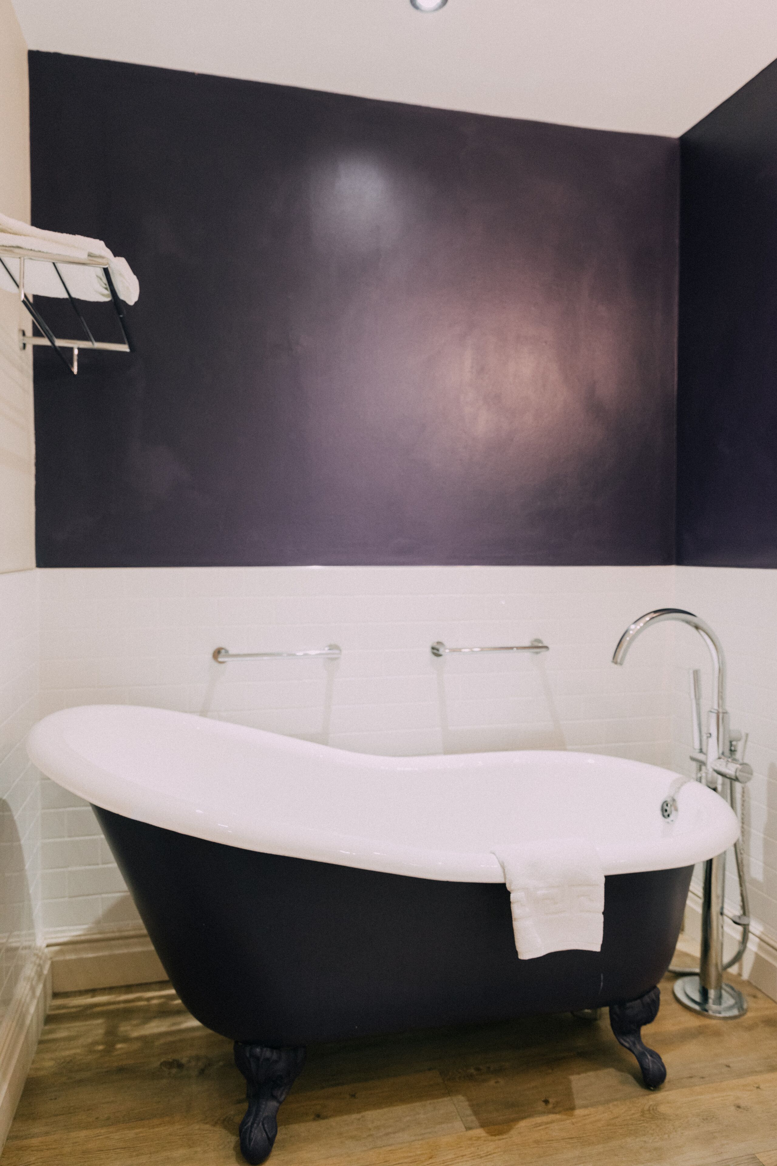 A modern bathroom with a freestanding bathtub, white tiled walls, and a dark accent wall.