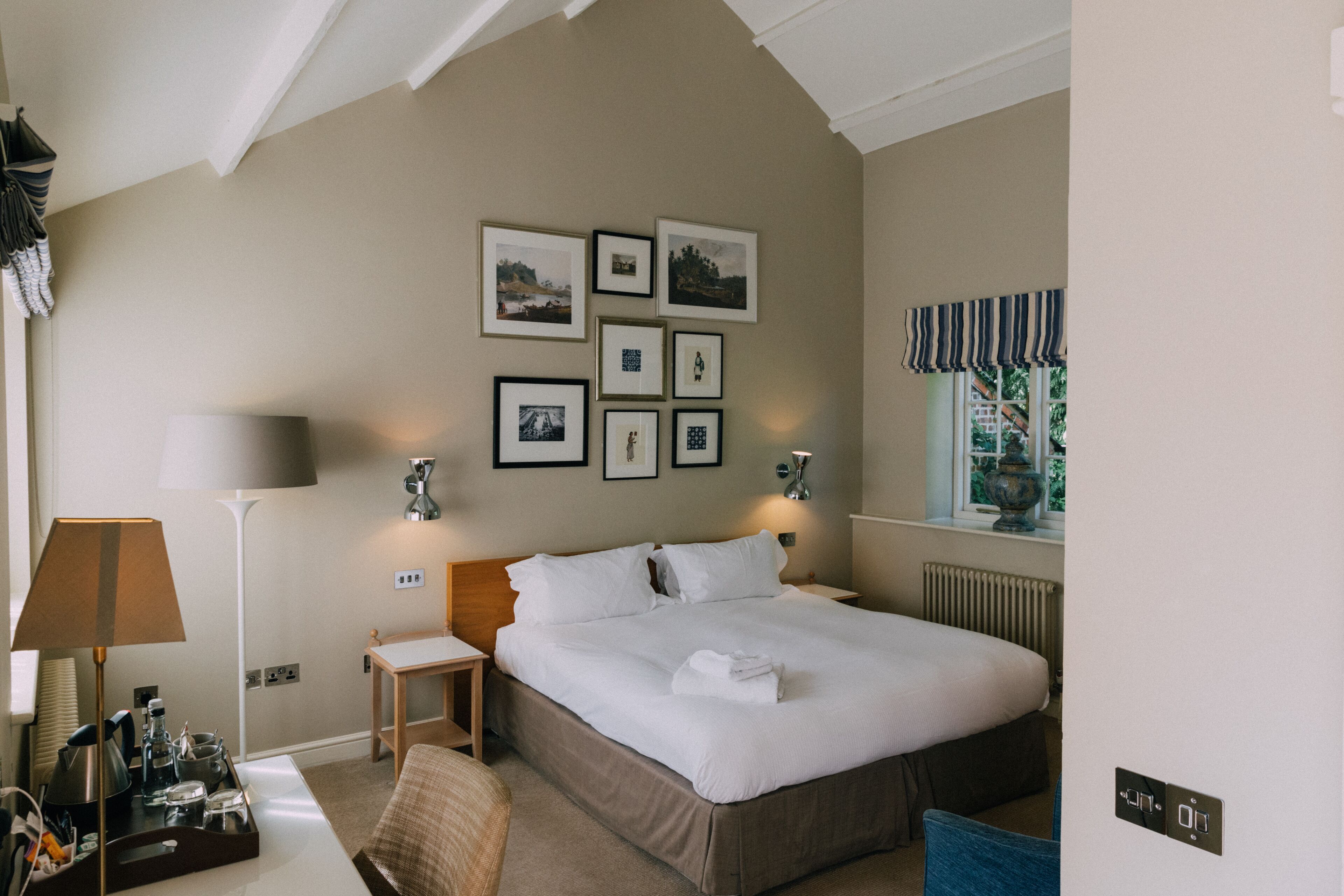 A hotel room with a large bed, bedside tables, a desk with a lamp, and framed pictures on the wall.