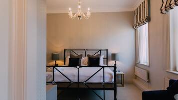 A bedroom with a bed, bedside lamps, a chandelier, a radiator, and a window with curtains.