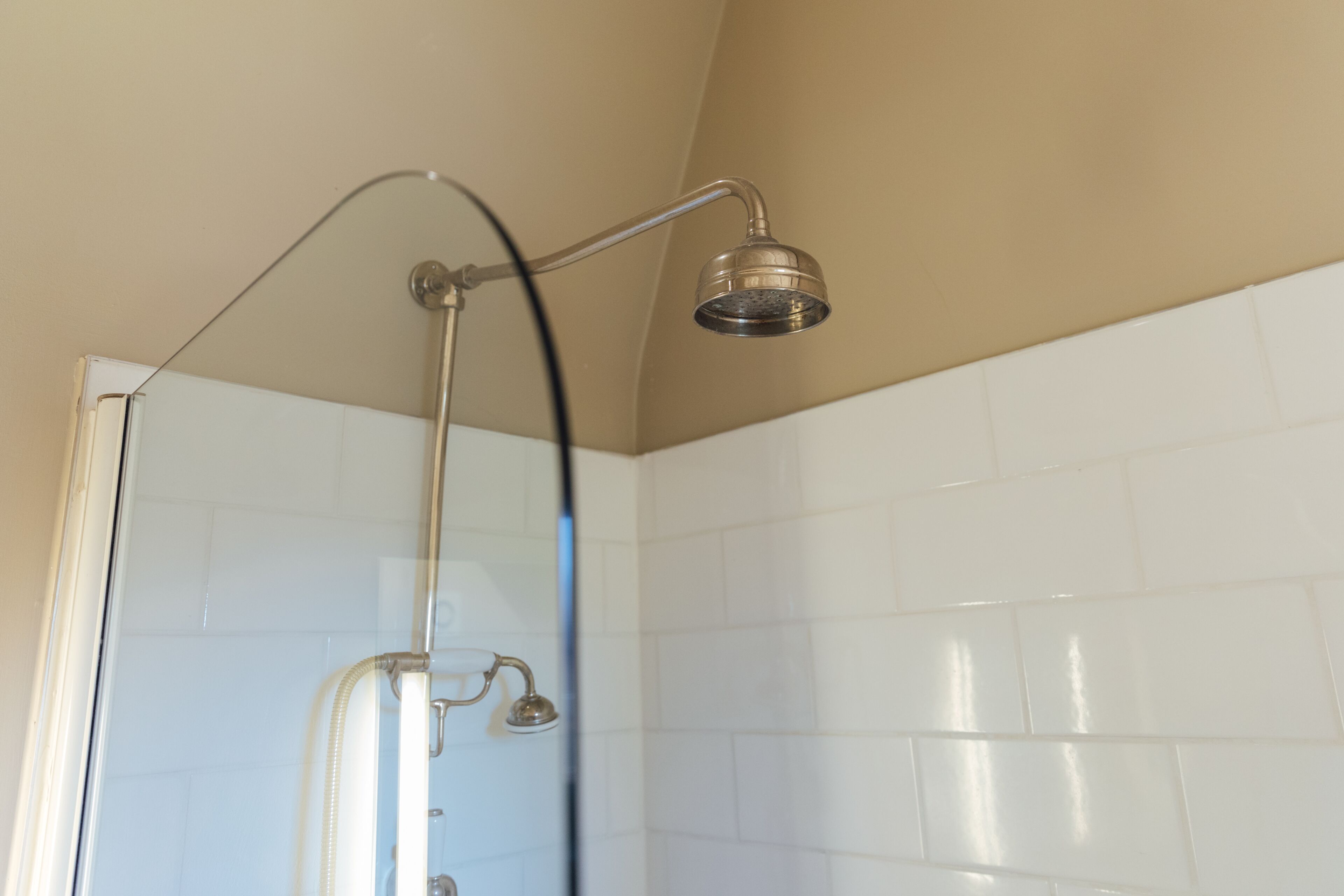 Une douche équipée d’un pommeau de douche à main et d’un robinet fixé au mur.