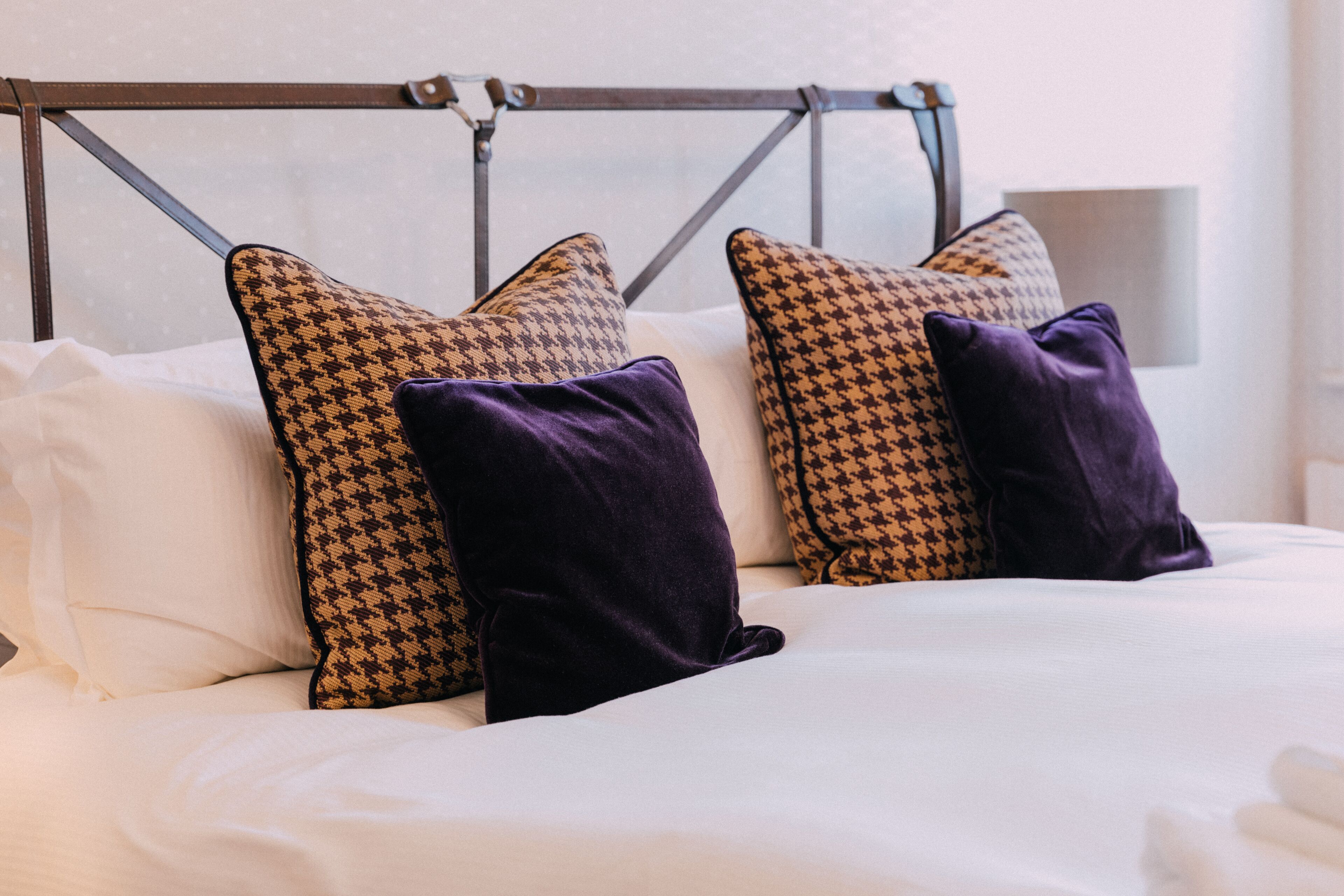 A bed with white bedding, two patterned pillows, and a metal headboard.