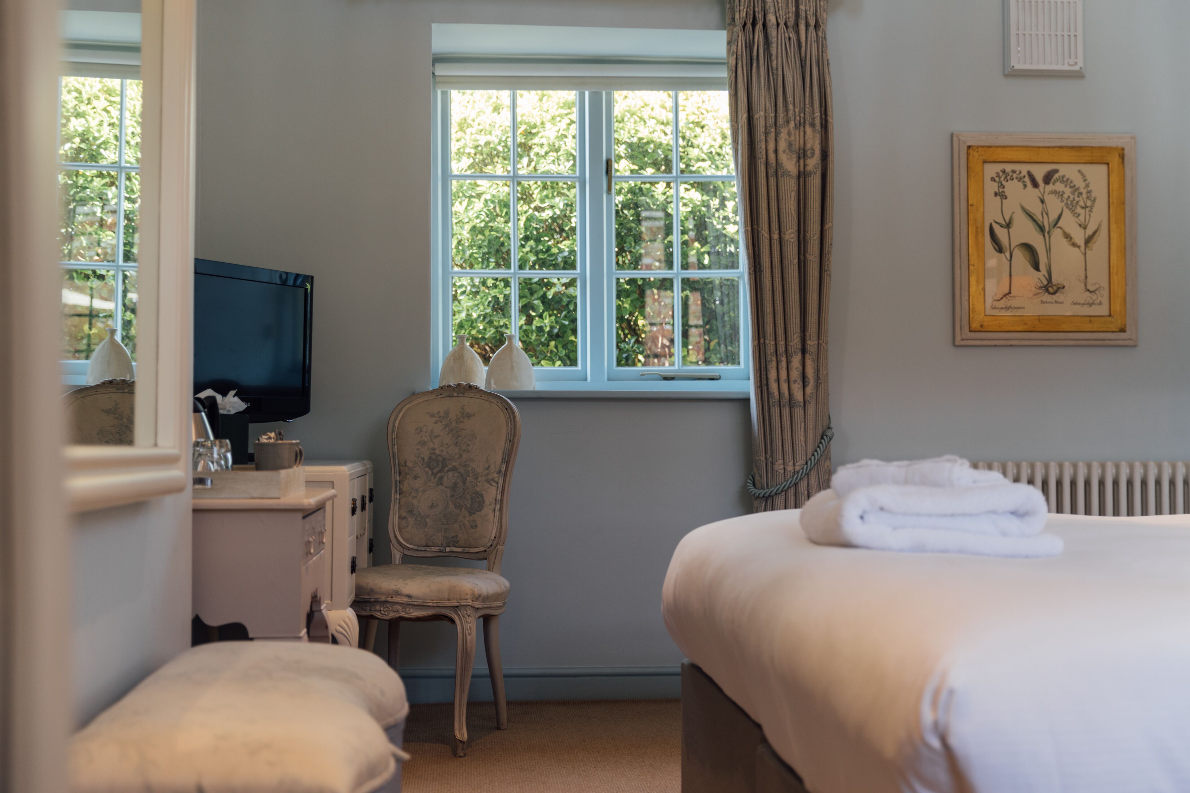 A bedroom with a bed, a chair, a desk with a television, and a window with curtains.