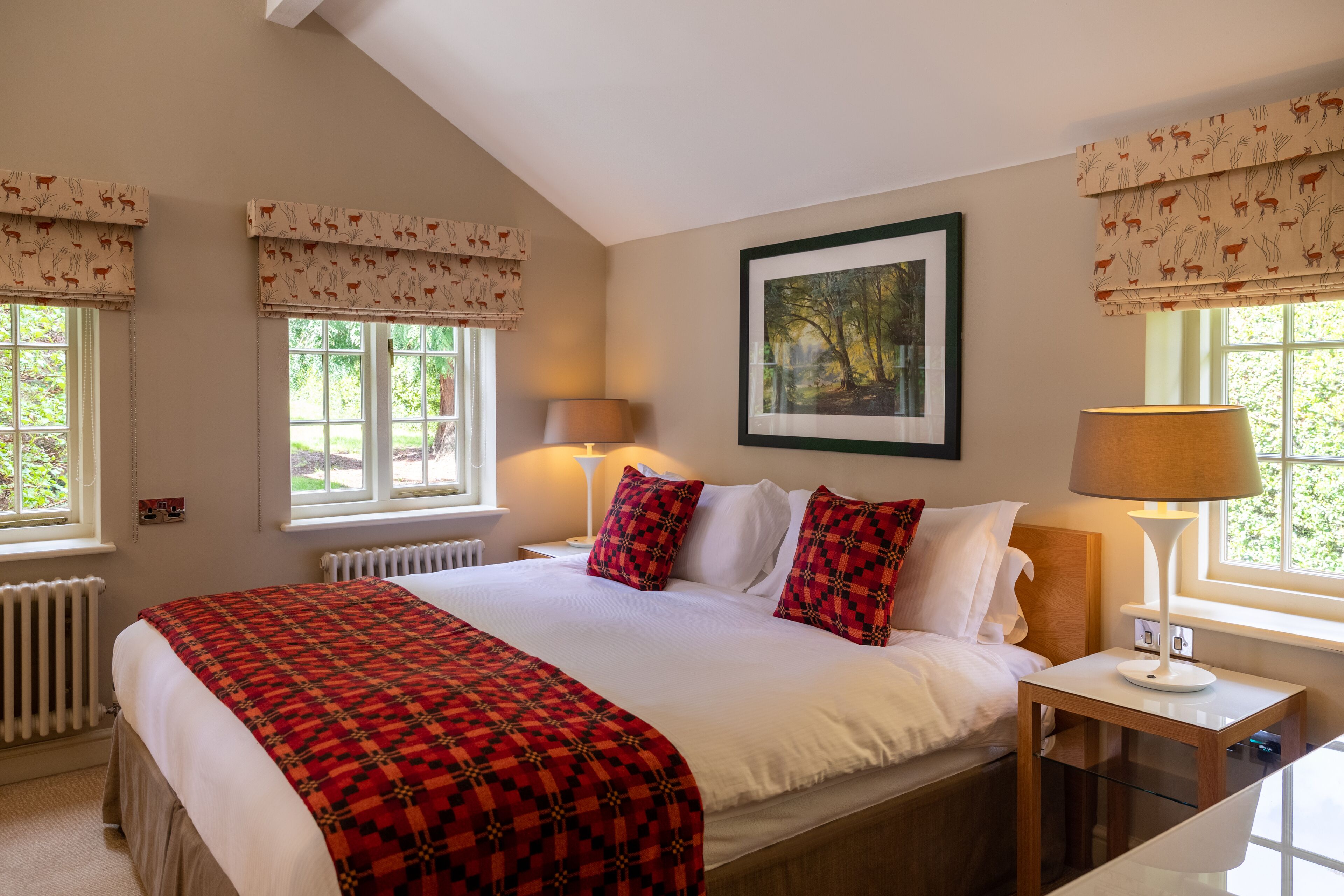 A bedroom with a large bed, two bedside lamps, a framed picture on the wall, and windows with patterned curtains.