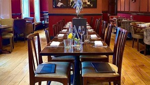A formal dining room with a long table set for multiple guests, a chandelier, and framed portraits on the wall.