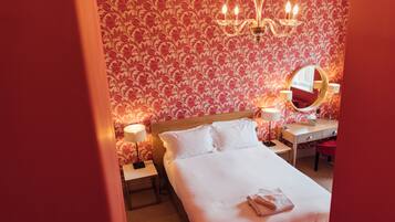 Een hotelkamer met een groot bed, twee nachtkastjes met lampen, een ronde spiegel en een kroonluchter.