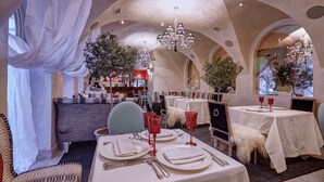 Un restaurante con manteles blancos, copas rojas y un candelabro.