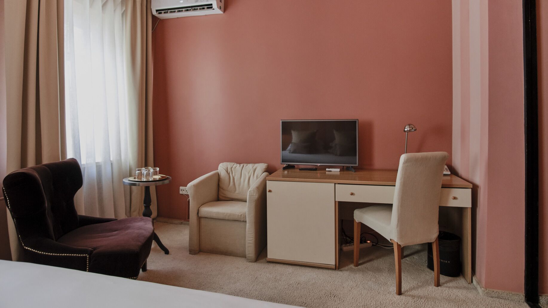 A hotel room with a desk, two chairs, a television, and a small table with glasses.