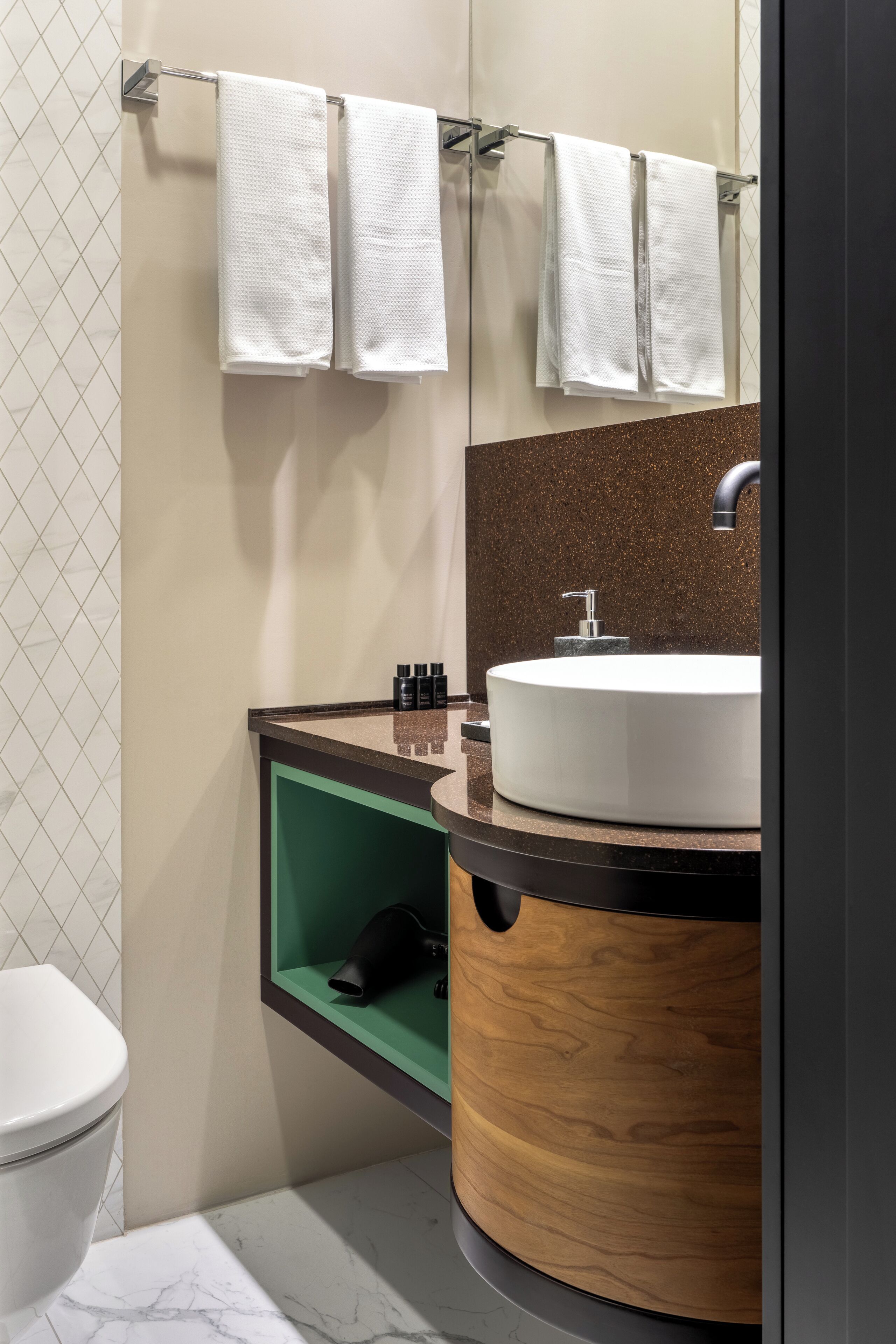 Une salle de bain moderne avec des toilettes blanches, un meuble-lavabo en bois et un porte-serviettes avec trois serviettes blanches.