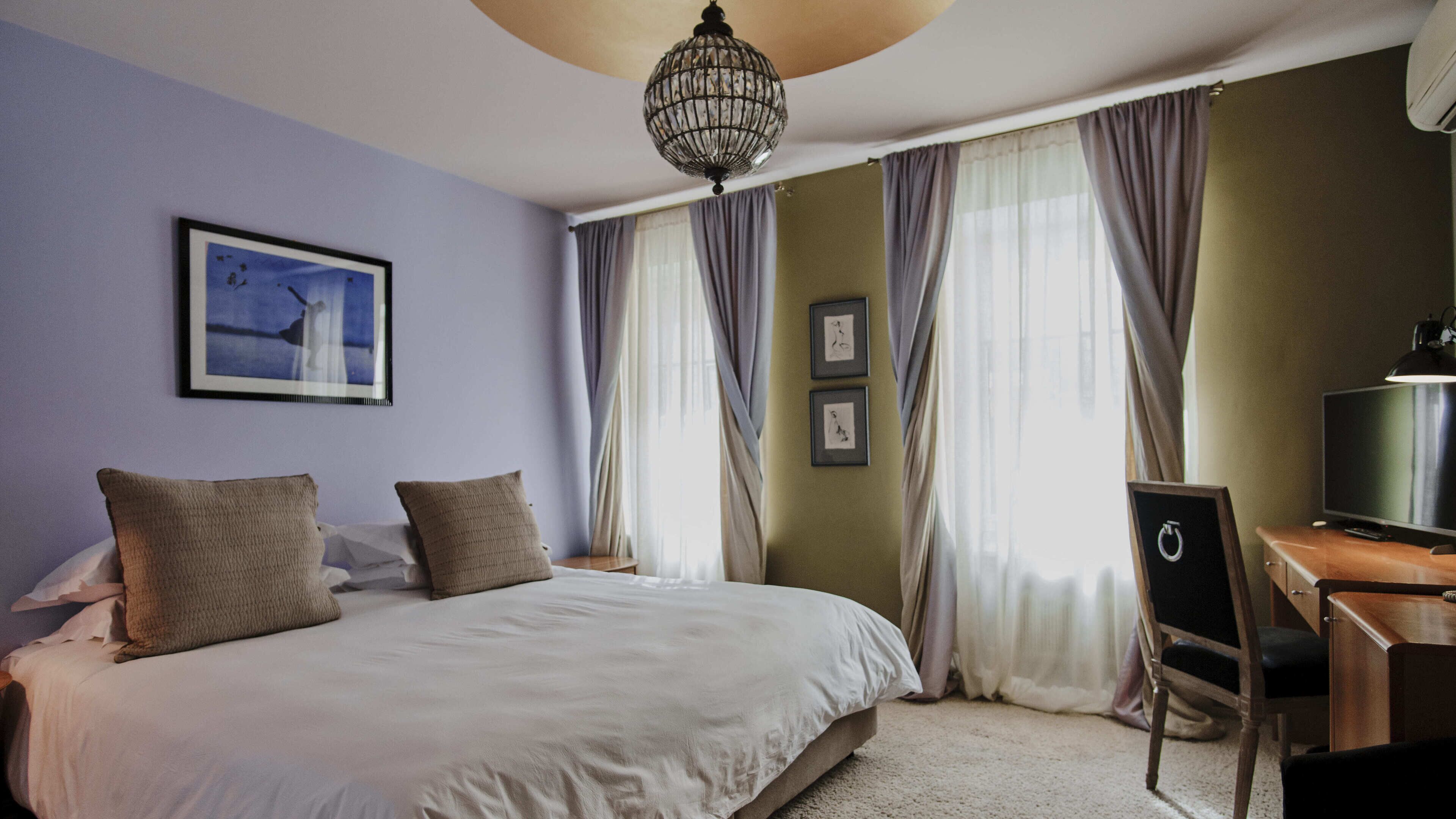A neatly made bed with two pillows, a desk with a chair, a television, and a chandelier.