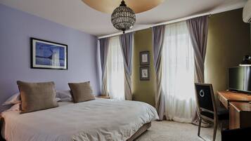 A neatly made bed with two pillows, a desk with a chair, a television, and a chandelier.