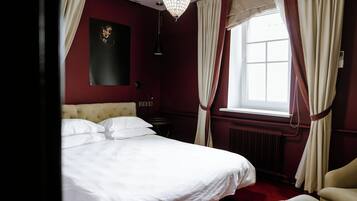 Uma cama bem arrumada com lençóis brancos, cabeceira estofada e piso coberto por um tapete vermelho.