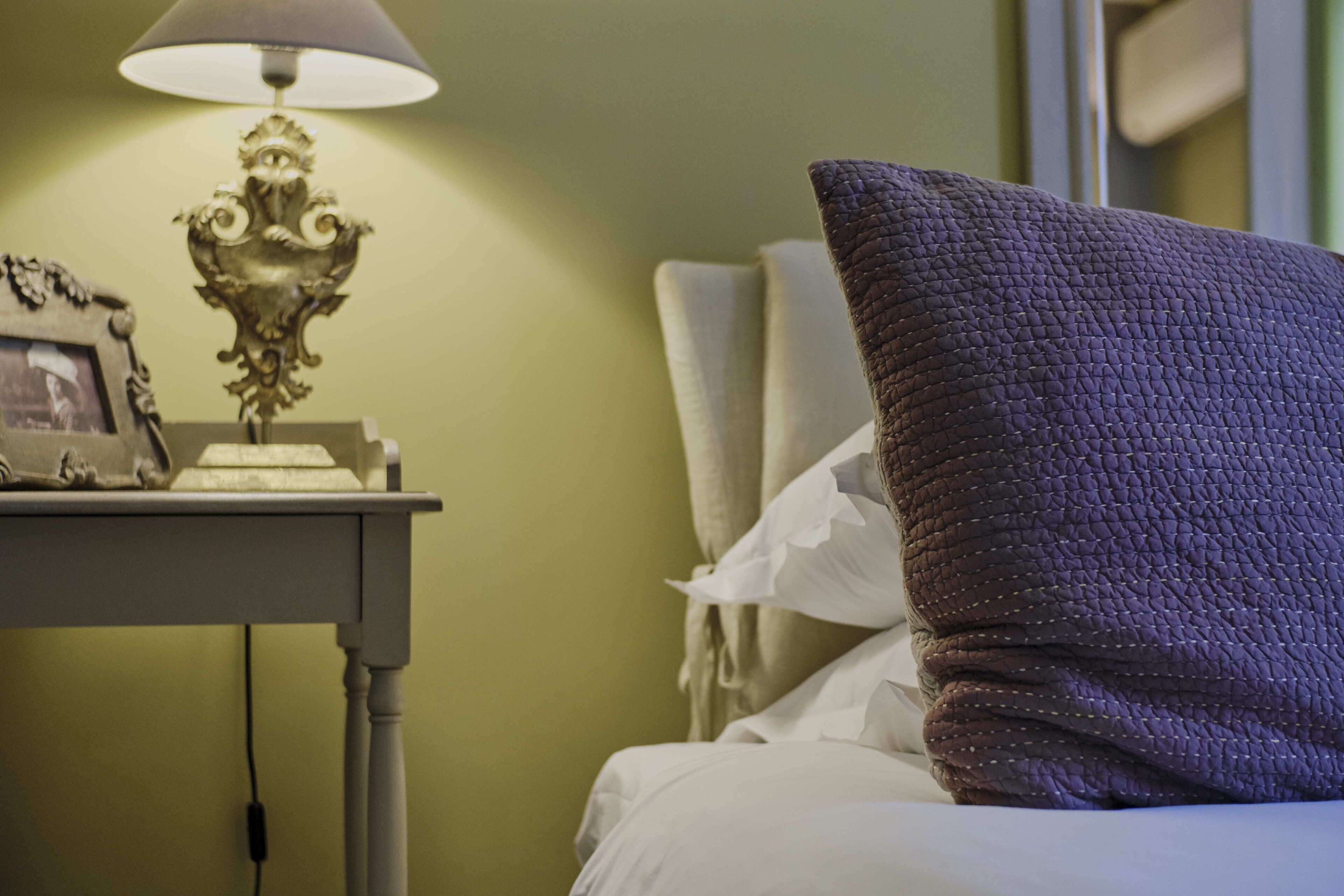 Een netjes opgemaakt bed met een gestructureerd kussen en een nachtkastje met een lamp en een fotolijst.