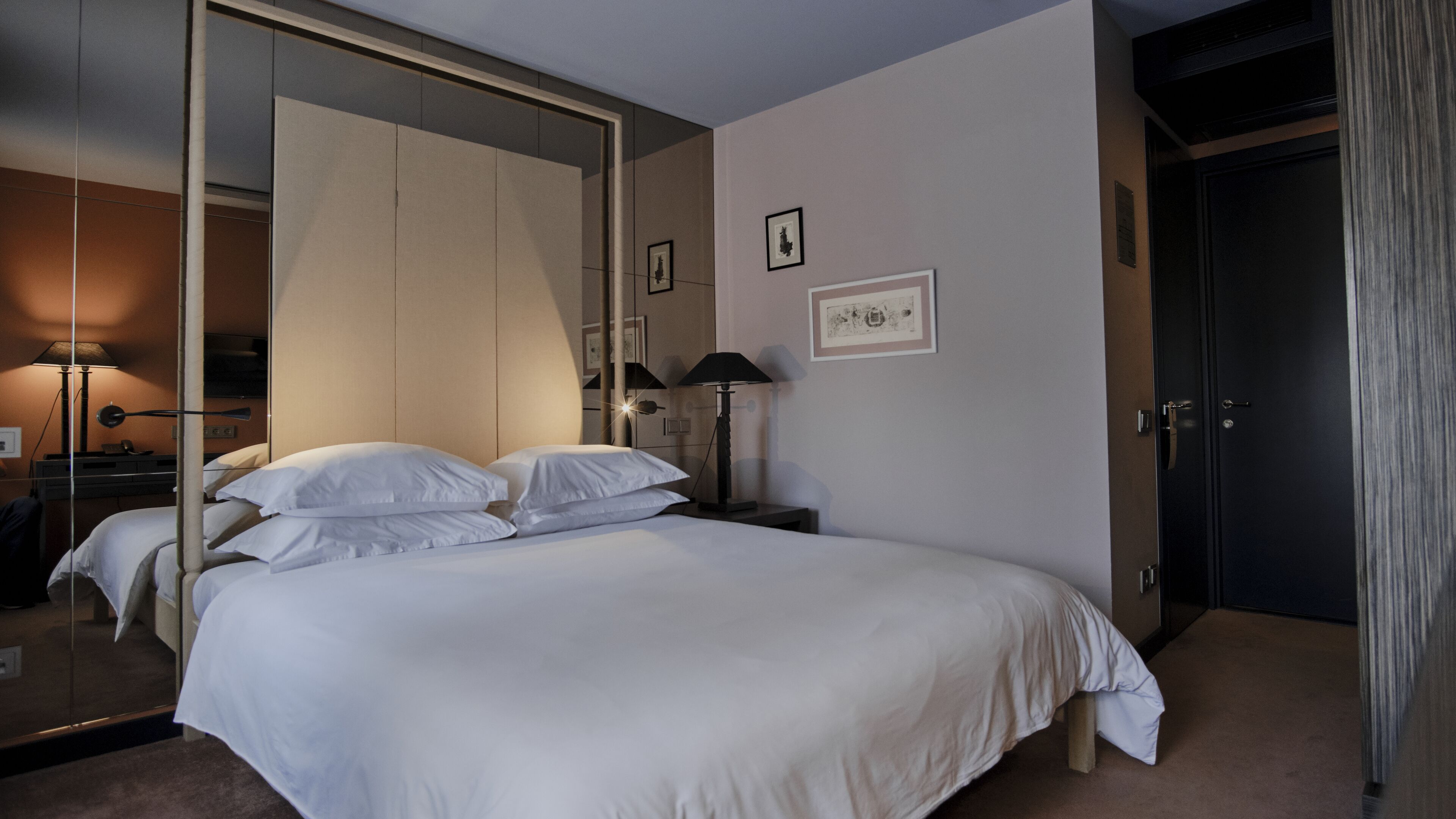 A hotel room with a large bed, a bedside table with a lamp, a mirror, and a door.