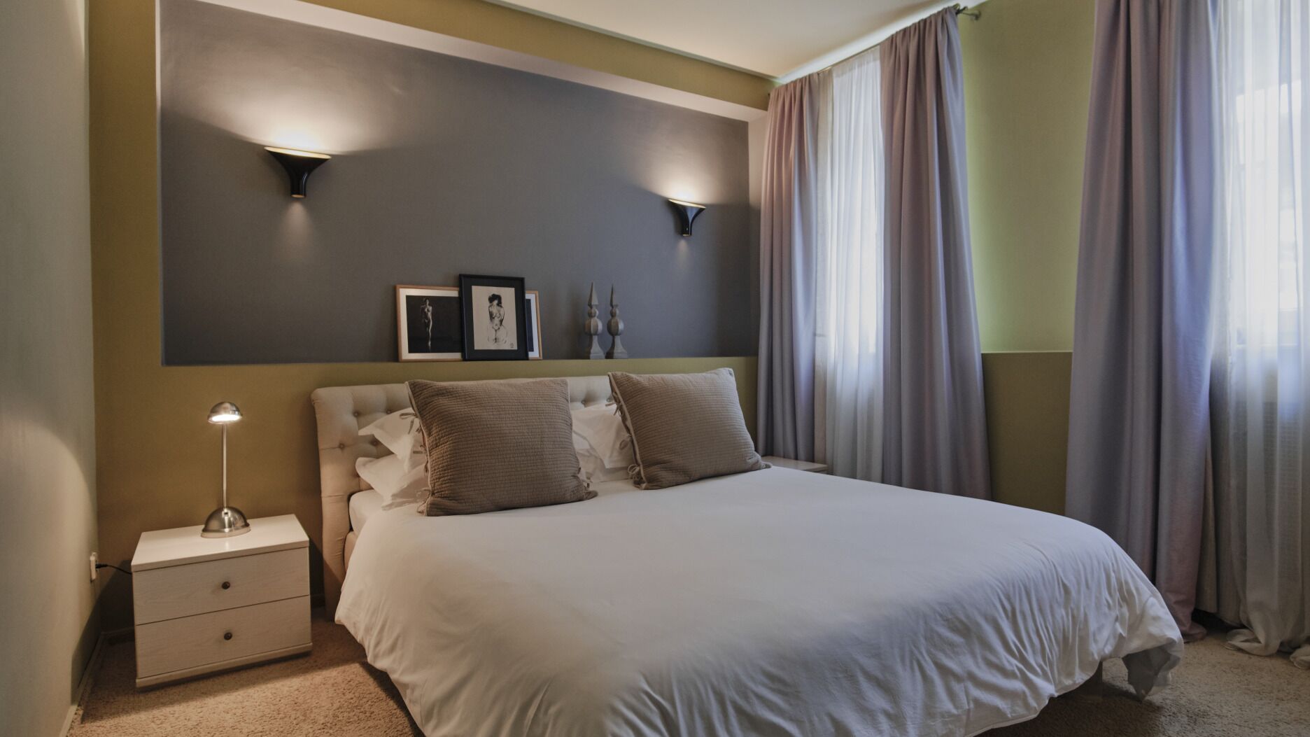 A neatly arranged bedroom with a bed, bedside tables, and wall-mounted lighting.