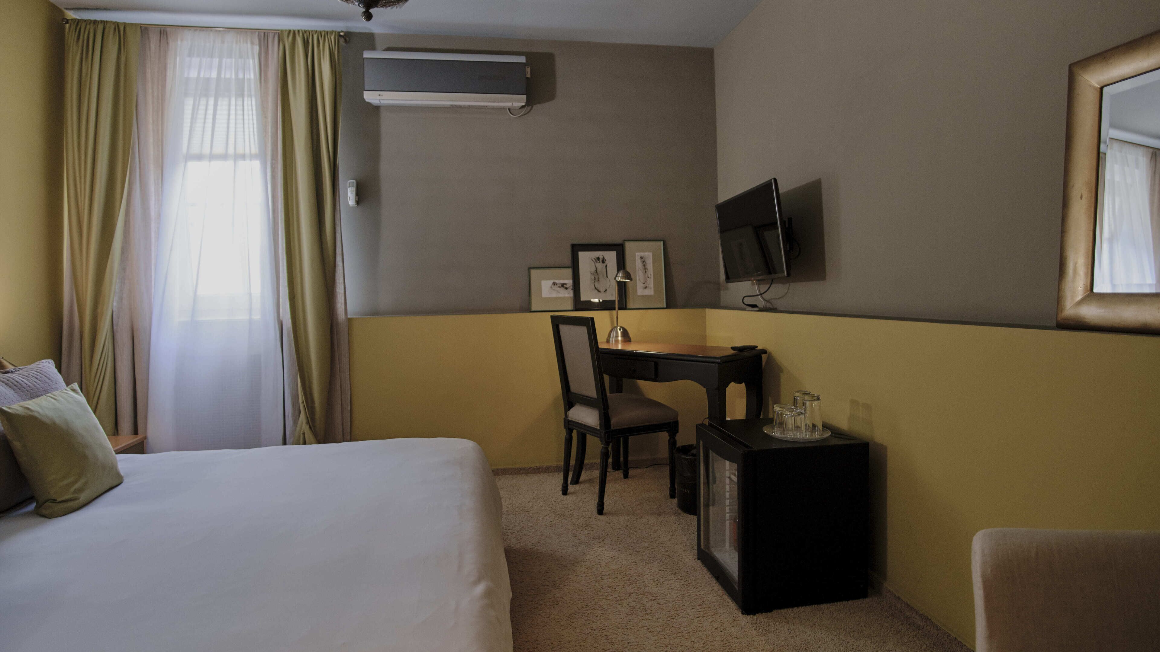Una habitación de hotel con una cama, un escritorio con una silla, un televisor y una mesita con vasos.