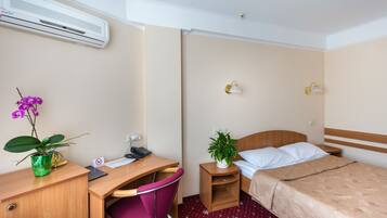 A hotel room with a desk, chair, bed, bedside tables, and a potted plant.